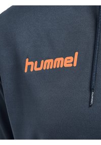 Sweat-shirt bleu foncé en tissu texturé, avec un logo orange "hummel" sur le devant et un col zippé.