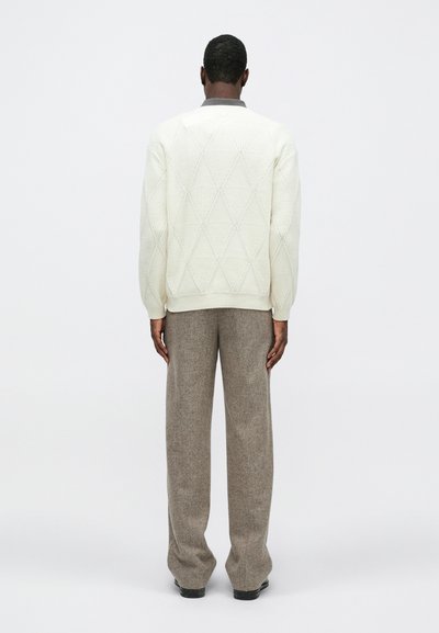 Pulover bărbați din tricot ușor în crem deschis, cu model în diamant, asortat cu pantaloni largi de culoare bej închis. Puloverul are guler rotund și manșete ribelate.