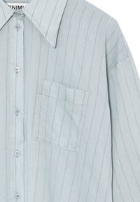 Světle modrá košile na knoflíky vyrobená z texturované látky. Má vertikální pruhy, velký límec a jednu náprsní kapsu.
