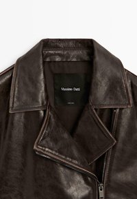 Braune Lederjacke mit weitem Revers, Frontreißverschluss und weicher, strukturierter Oberfläche. Das Etikett mit der Aufschrift "Massimo Dutti" befindet sich innen am Kragen.