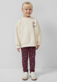 Kremowa bluza z napisem "HAVE A GREAT DAY", zestawiona z bordowymi legginsami w kwiatowe wzory oraz białymi trampkami.