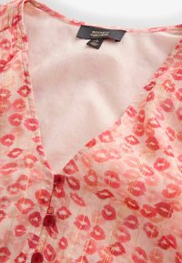 Blusa rosa con stampa a motivo di labbra rosse, strisce verticali dorate, bottoni rossi e etichetta "Rockett St George" all'interno dello scollo.