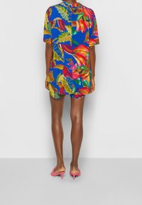 Abito corto a maniche corte colorato con un design a patchwork che presenta motivi floreali tropicali e foglie su uno sfondo blu.