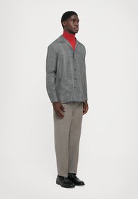 Hallide šedast ruuduline jaki siniste ja oranžide joontega, nupuga kinni pandud ja kahekaupa ees, seljas punane kõrge kaelusega särk ja hallid püksid.