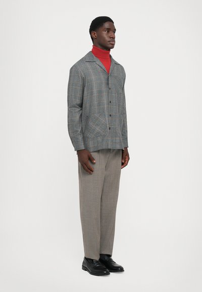 Hallide šedast ruuduline jaki siniste ja oranžide joontega, nupuga kinni pandud ja kahekaupa ees, seljas punane kõrge kaelusega särk ja hallid püksid.