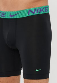 Fekete sportos boxer alsó zöld és lila csíkos rugalmas derékkal, amelyen lila Nike logó és egy kis zöld swoosh található a lábon.