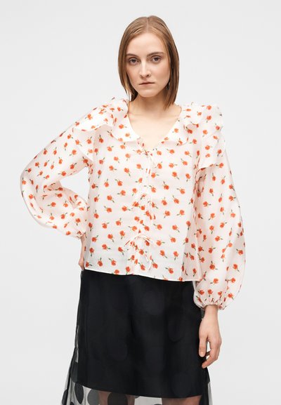 Λουλουδάτο μπλουζάκι με φουσκωτά μανίκια, κατασκευασμένο από ελαφρύ ύφασμα, με ροζ βάση, κόκκινο σχέδιο λουλουδιών και κορδονάκια στον λαιμό και το τελείωμα.