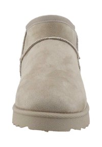 Botte de cheville en suede beige avec un bout arrondi, des coutures le long du bord, une semelle en caoutchouc texturée et un panneau élastique à la cheville.