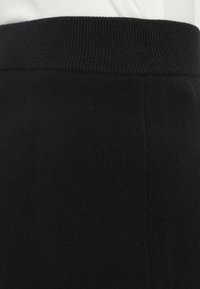 Jupe en tricot noire avec une texture lisse, une taille élastique et des détails de couture subtils. Le tissu est doux et flexible.