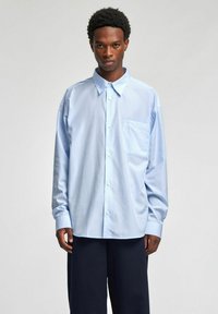 Lyseblå stripete skjorte med knappelukking og lomme, med en avslappet passform og lange ermer, laget av et glatt stoff.