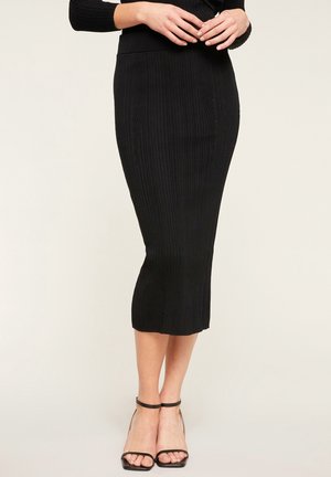 Schwarzer, gerippter Strick-Midi-Rock mit einer figurbetonten Silhouette, hoher Taille und subtilen Details entlang der Nähte, kombiniert mit schwarzen Riemchen-Heels.