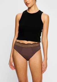 Culottes en coton marron taille haute avec une taille en dentelle, présentant un bord festonné et une texture lisse. Associées à un débardeur noir.