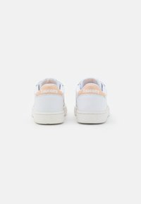 Scarpe in pelle bianca con design a punta bassa, caratterizzate da un accento rosa chiaro sul tallone e una suola di crema testurizzata. Logo "Saucony" sul retro.