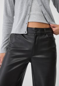 Zwarte faux leren broek met een gladde textuur, hoge taille, voorzakken en een knoopsluiting. Grijze geribbelde cardigan met knopen.