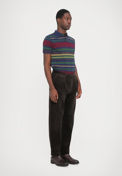 Polo cu dungi în nuanțe de navy, măru și verde cu guler; asociat cu pantaloni din corduroy de culoare maro închis și cizme maro închis.