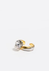 Anillo de metal con una gran piedra de cristal, con una banda de oro y un acento de plata, diseñado para ser abierto y ligeramente curvado.