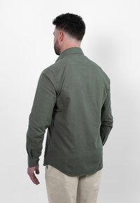 Olijfgroene button-up shirt met een kraag, lange mouwen en zichtbare stiksels, gecombineerd met lichtbeige broek.