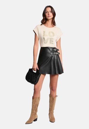T-shirt beige avec "LOVE" en paillettes, jupe plissée en cuir noir avec doubles boucles, sac à main noir texturé, et bottes hautes en daim beige.