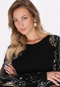 Pulover negru cu mâneci decorate cu paiete în modele de valuri aurii, argintii și negre. Design lung, ajustat, cu decolteu rotund.
