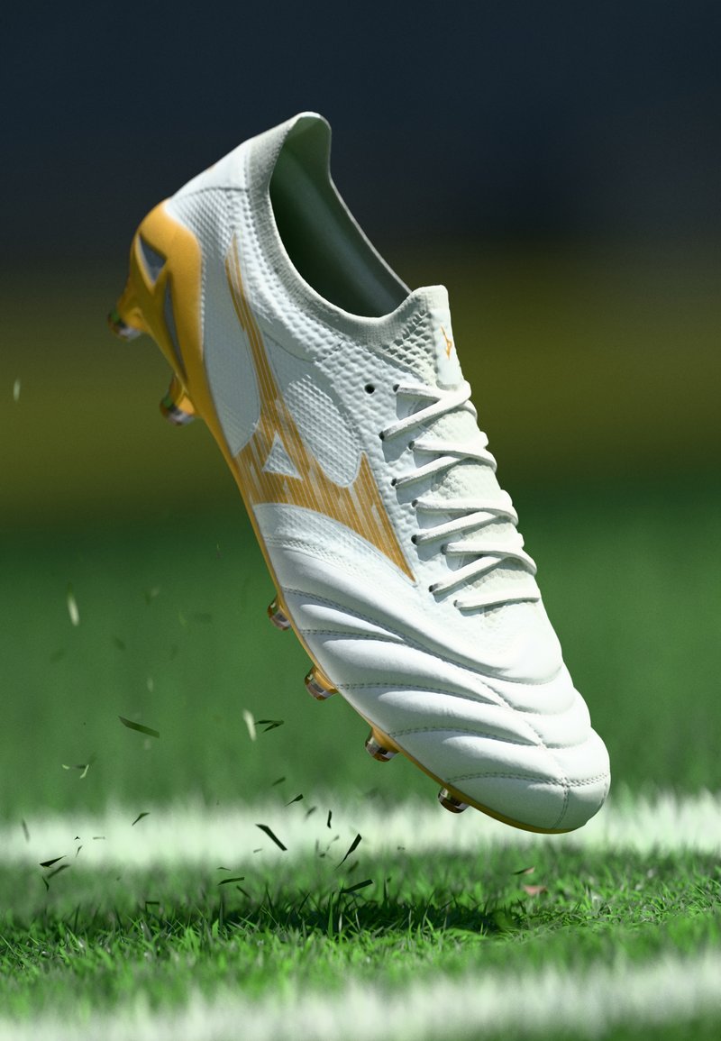 White football boot with yellow accents, textured upper, and laces. Cleats visible underneath; hovering above a grassy field.