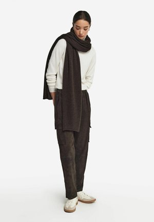 Lys beige trøje, mørkebrun tørklæde og mørke cargos, kombineret med hvide sneakers. Strukturerede materialer inkluderer strik og ruskind.