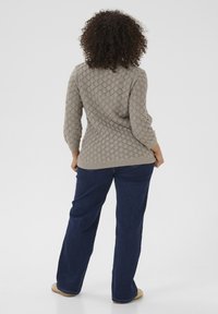 Lichtgrijze gebreide trui met een gemêleerd patroon, driekwartmouwen en een ontspannen pasvorm, gecombineerd met donkerblauwe uitlopende jeans.
