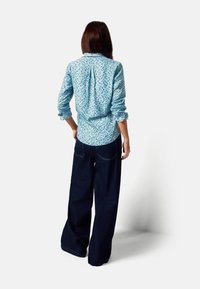 Lichtblauw overhemd met bloemenpatroon, lange mouwen, een plooi aan de achterkant en opgerolde manchetten, gecombineerd met loszittende donkeren denim broek.