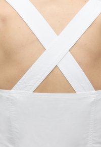 Κοντινό ενός γυμνού πίσω μέρους ενός ατόμου με λευκούς ιμάντες ρούχων που διασταυρώνονται σε σχήμα Χ.