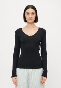 Haut noir à manches longues avec une texture côtelée, décolleté en V et dentelle le long du col. Design ajusté, associé à un pantalon de pyjama léger à rayures.