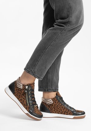 Beine in grauen Jeans und leo-print hohen Sneakern mit schwarzen Akzenten, beige Knöchelsocken, stehend vor weißem Hintergrund.
