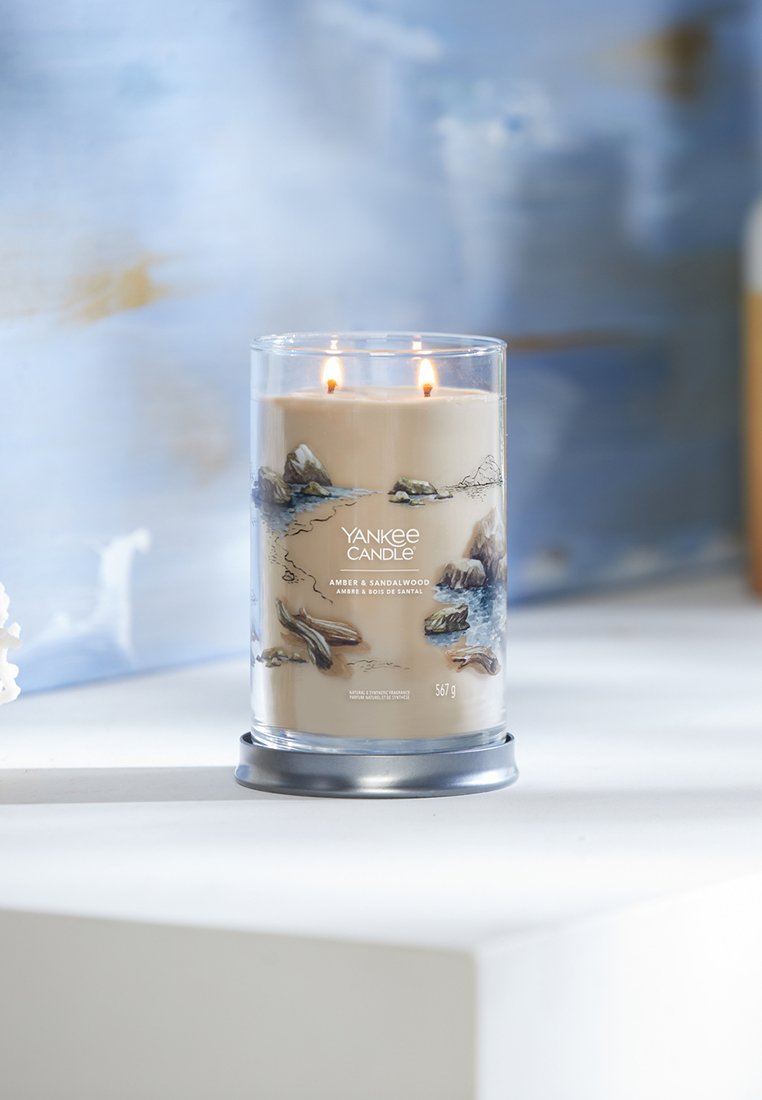 Yankee Candle en un frasco de vidrio transparente, con cera beige y dos llamas. Decorado con un diseño inspirado en la naturaleza y una base de metal plateado.