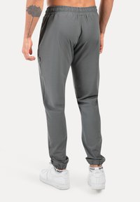 Grå træningsbukser med elastisk talje og ankelfløjter, der har sidelommer og en glat, fin tekstur. Båret med hvide sneakers.