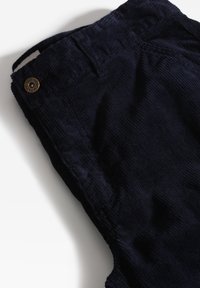 I pantaloni in corduroy blu navy presentano una superficie testurizzata, un bottone con il logo del marchio e cuciture visibili lungo la vita.