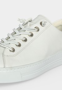 Zapatilla blanca de cuero con suela blanca gruesa y cordones distintivos en forma de lazo pasados por ojales metálicos.