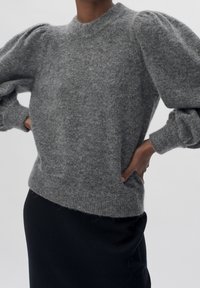 Szary sweter dziergany z okrągłym dekoltem, bufiastymi rękawami i miękką, puszystą fakturą. Połączony z czarną spódnicą dla kontrastu.