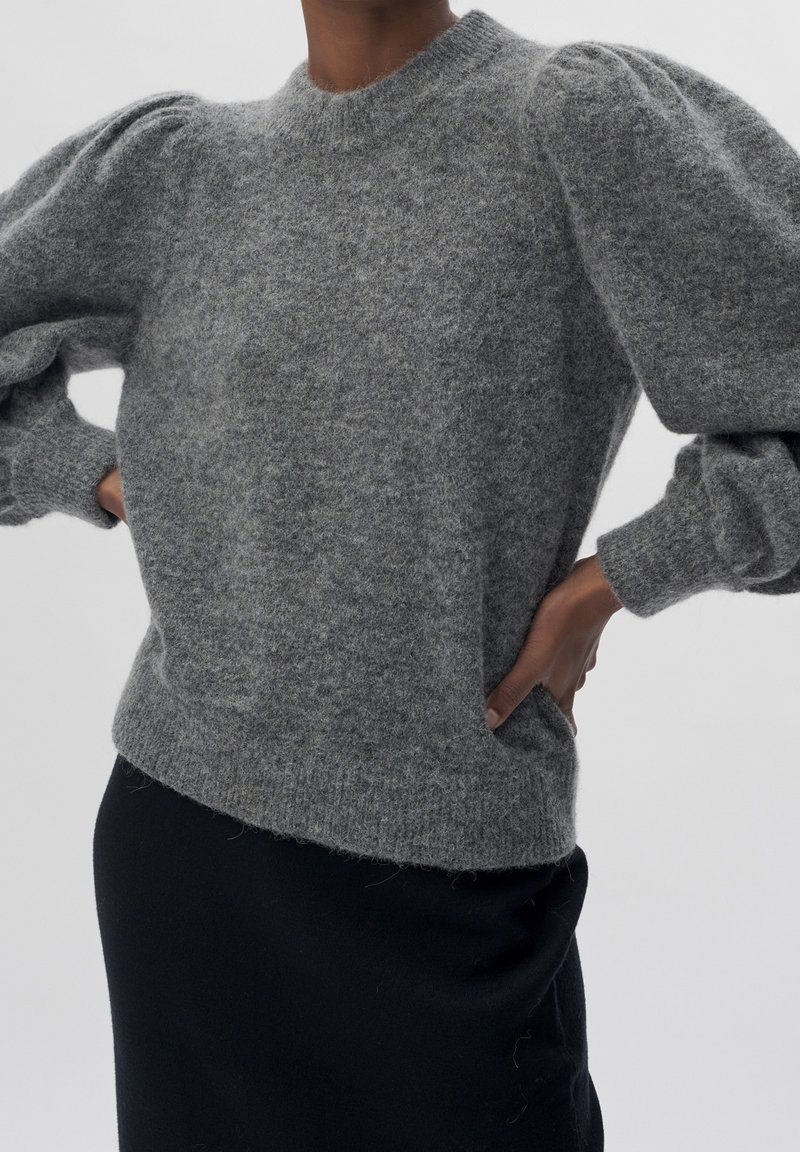 Szary sweter dziergany z okrągłym dekoltem, bufiastymi rękawami i miękką, puszystą fakturą. Połączony z czarną spódnicą dla kontrastu.