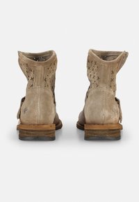 Botines de ante en beige claro con diseño perforado y un tacón bajo apilado. Presentan una hebilla lateral y detalles de costura.