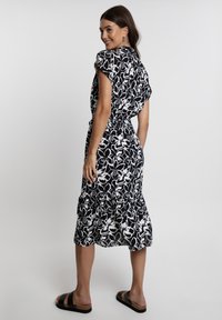 Schwarz-weißes Blumen-Midikleid mit kurzen Ärmeln, volantsaum und tailliertem Schnitt. Kombiniert mit schwarzen flachen Sandalen.