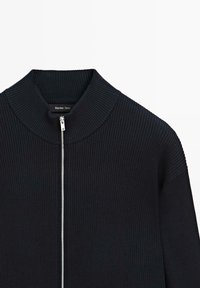 Giacca nera a coste con zip argentata e colletto alto, mostrata frontalmente su uno sfondo bianco.
