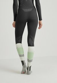 Zwarte sportlegging met gestructureerde accenten, gecombineerd met meerkleurige kniekousen in wit, groen en grijs, met blokpatronen.