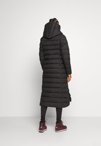 Giacca imbottita nera con cappuccio, con design lungo e trapuntato. Indossata sopra leggings e stivaletti bordeaux con suole bianche.