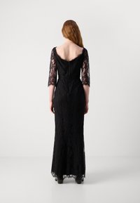 Robe de soirée en dentelle noire avec de longues manches en dentelle, un dos en V, et une silhouette ajustée avec un ourlet évasé. Motif texturé sur l'ensemble.