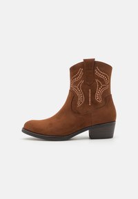 Bottine en daim marron avec un bout pointu, des motifs de couture décoratifs et un petit talon empilé. Elle possède des languettes sur le côté pour un enfilage facile.
