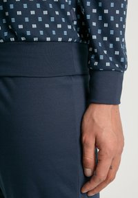 Marineblauw sweatshirt met geometrische witte en lichtblauwe ontwerpen, voorzien van een bijpassende tailleband en manchetten.