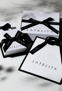 Hvide gaveæsker med sorte bånd, der pryder "LATELITA" i fed skrift. Æskerne har varierende størrelser og skarpe rektangulære former.