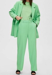 Blazer su misura verde menta e pantaloni a gamba larga abbinati a una maglietta coordinata. Tessuto morbido, vestibilità comoda e design minimalista.