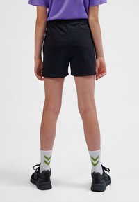 Pantaloncini neri con una texture liscia e vita elasticizzata, abbinati a calzini bianchi con motivi a chevron verdi e scarpe sportive nere.