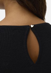 Haut en tricot noir avec un détail en trou de serrure à l'arrière, maintenu par un petit accent en forme de cœur doré près de l'encolure.