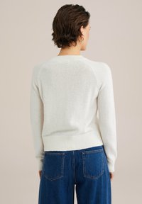 Krämfärgad stickad tröja med ribbade manschetter och midja, som har raglanärmar och en mjuk, texturerad yta. Tillsammans med blå jeans.