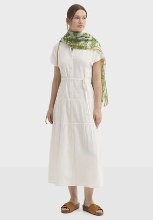 Robe blanche à boutons, avec une ceinture à la taille, un design à étages et des manches courtes, associée à une écharpe verte à motifs et des sandales marron à enfiler.